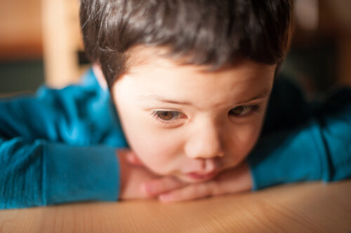 Niño triste y pensativo apoyado en la mesa.