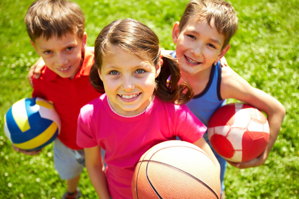 Enfants avec des ballons de football et des balles de différents sports.