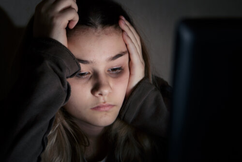En stressad tonårsflicka som tittar på en datorskärm i mörkret.