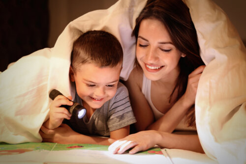 Madre e hijo leyendo un libro bajo las sábanas con una linterna.