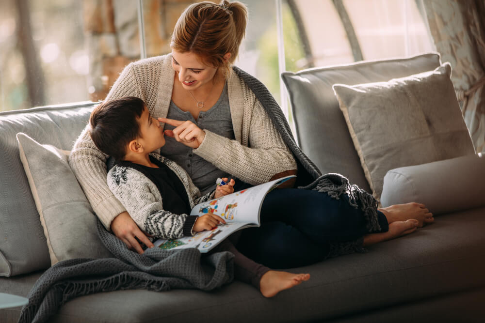 Une mère et son fils qui regardent un livre sur le canapé.