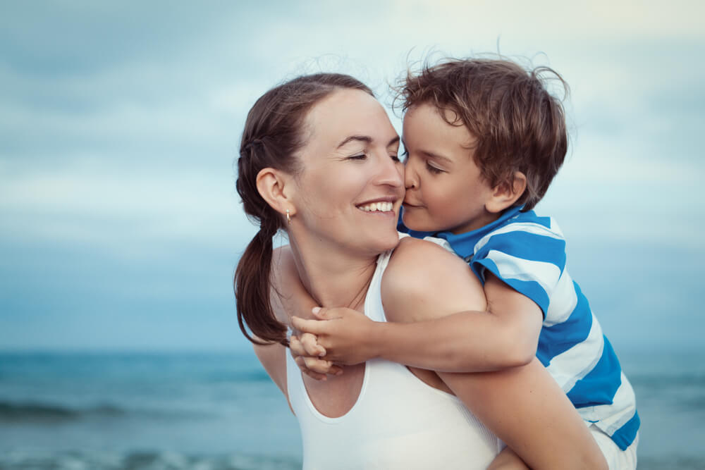 Madre pasando tiempo con su hijo en la playa, quien le da un beso.