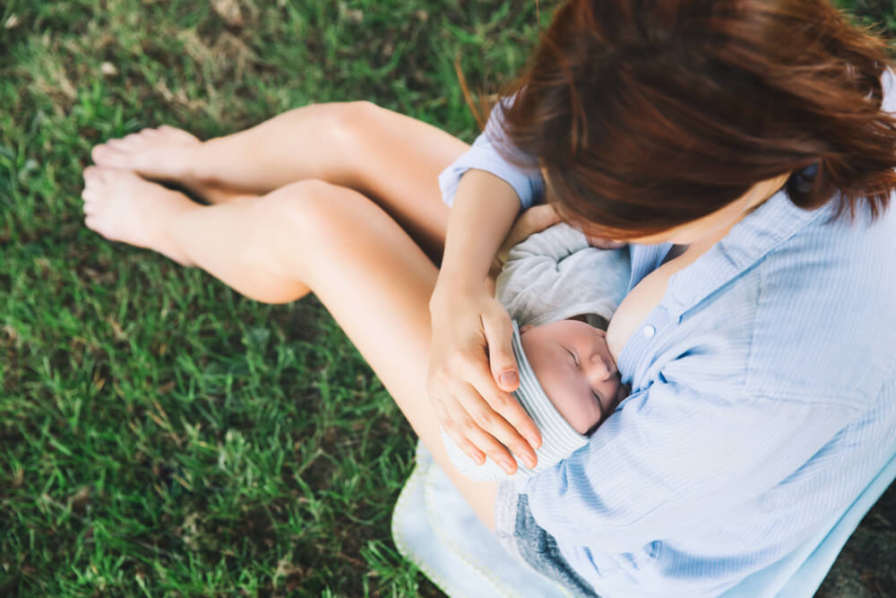 Une maman qui allaite son bébé assise dans l'herbe.