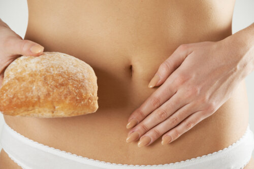 Mujer con un pan de la mano y dolor de barriga debido a la sensibilidad al gluten no celiaca que padece.