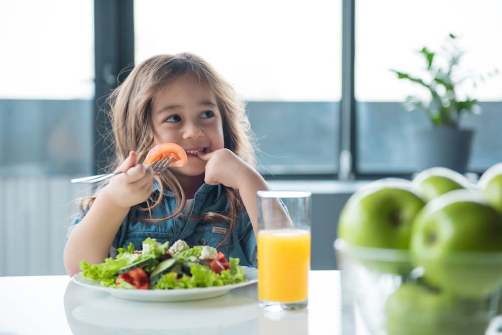 Niña comiendo una ensalada con buenos modales en la mesa.