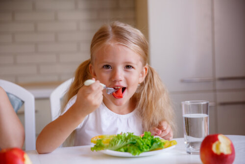 Niña comiendo con buenos modales en la mesa.