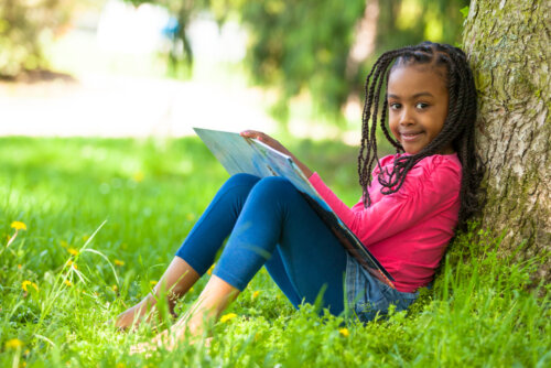 Niña apoyada en un árbol leyendo un libro.