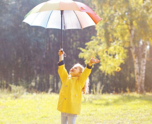 Niña disfrutando bajo la lluvia con un paraguas y un chubasquero.