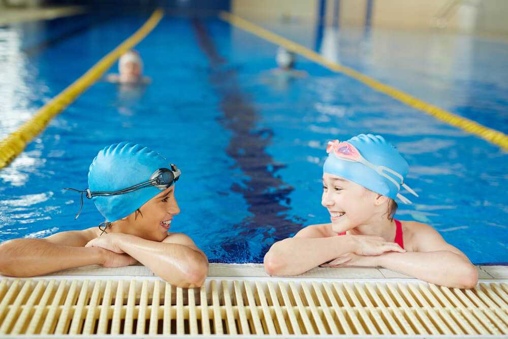 Two girls swimming at one another during swim class.