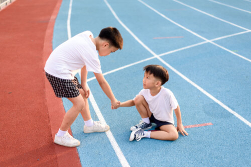 Niño ayudando a otro que se ha caído en las pistas de atletismo.