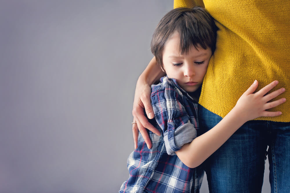 A child looking shy and hugging his mother at the hip.