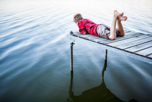 Niño tumbado en un muelle frente al agua para aprender el valor de la serenidad.