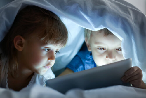 Niños viendo una película bajo las sábanas en un gadgets como es la tablet.