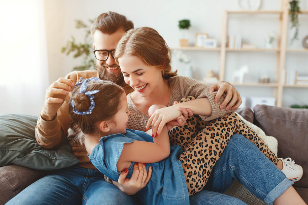 Padres haciéndole cosquillas a su hija en el sofá.