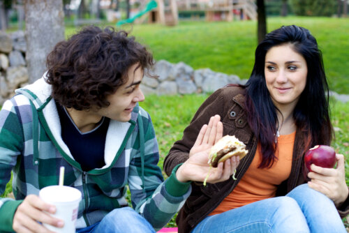 Chica rechazando una hamburguesa y comiendo una manzana debido a que padece ortorexia.