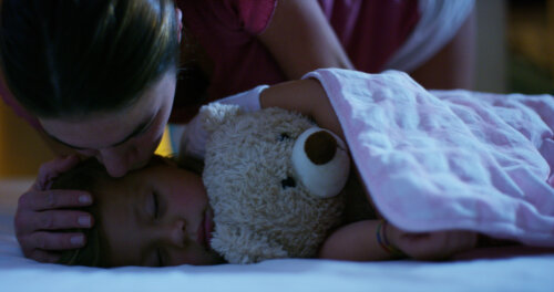 Madre dando un beso de buenas noches a su hija dormida.