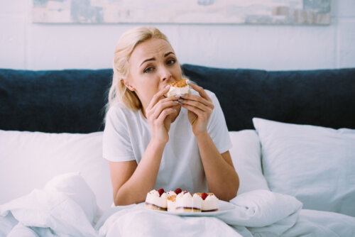 Mujer comiendo pasteles en la cama porque tiene ansiedad por la comida.