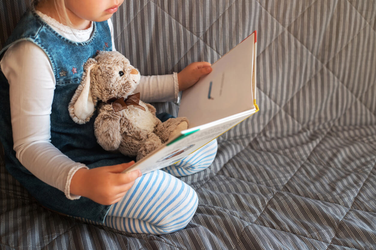 Niña leyendo un cuento su conejo de peluche por el Día Internacional del Libro Infantil.
