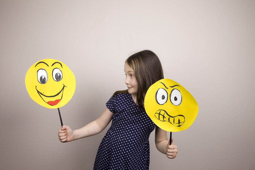 A child holding emoji signs representing happiness and frustration.