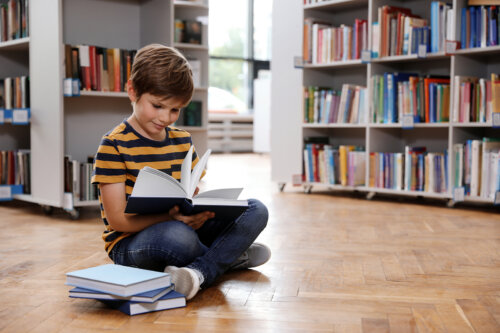 Niño leyendo un libro sentado en el suelo de la biblioteca.