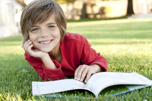 Garçon lisant un livre allongé sur l'herbe.