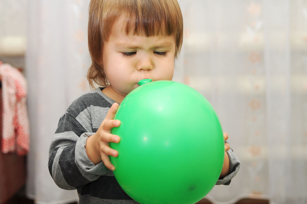 Menina soprando um balão para estimular a linguagem.