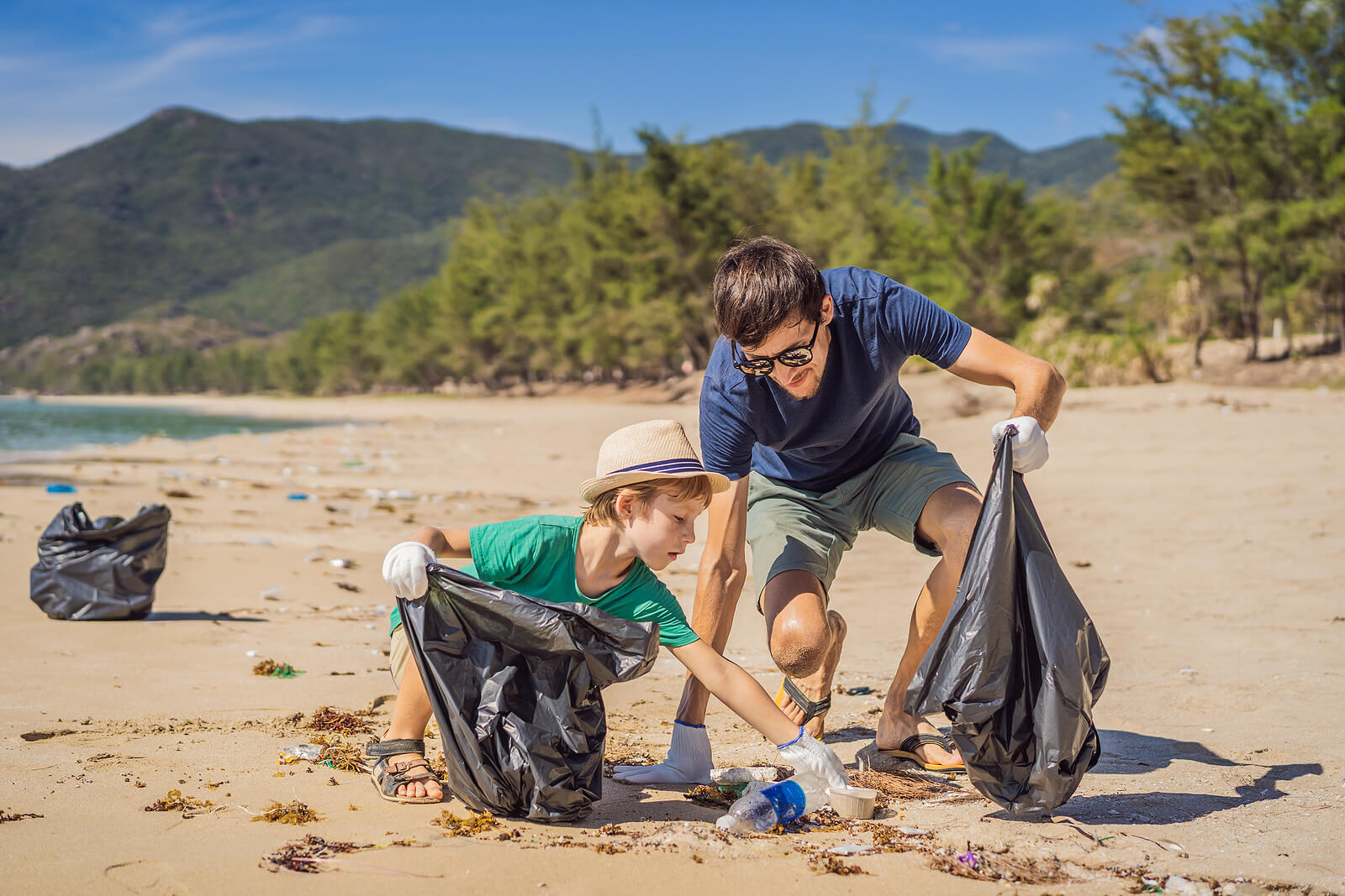 Padre e hijo recogiendo residuos y reciclando en la playa como parte de la educación medioambiental.