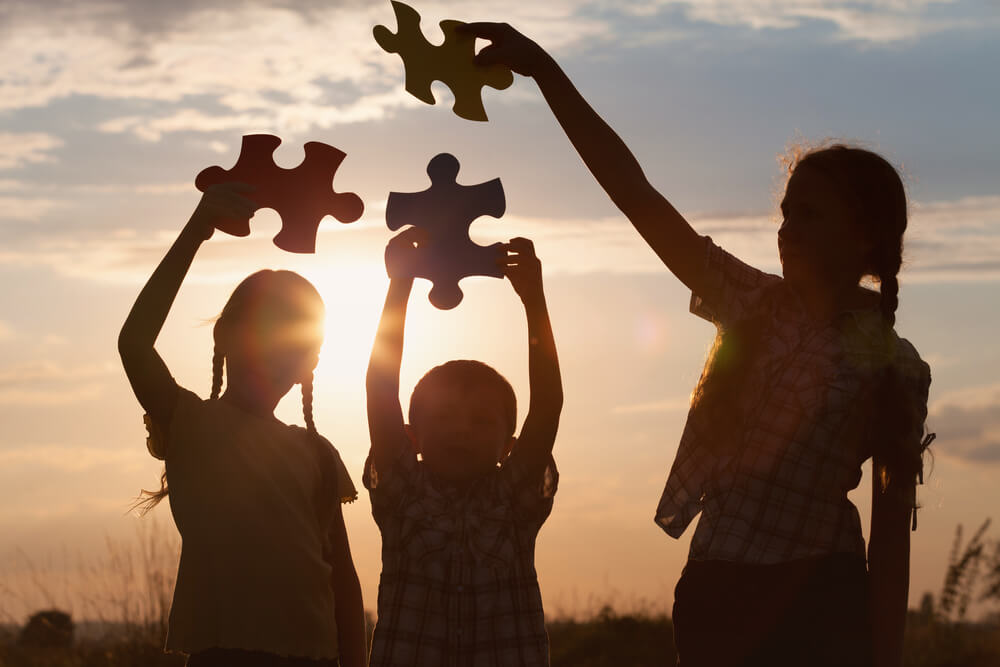 Tres hermanos con piezas de puzzle al atardecer.