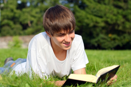 Chico joven leyendo uno de los libros para viajar en el tiempo tumbado en el césped.