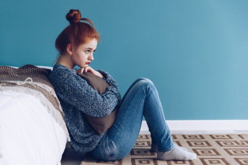 Adolescente triste sentada en el suelo de su habitación durante el confinamiento.