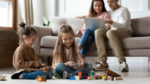 Hijas jugando mientras su padres hacen otras tareas en el sofá de casa.