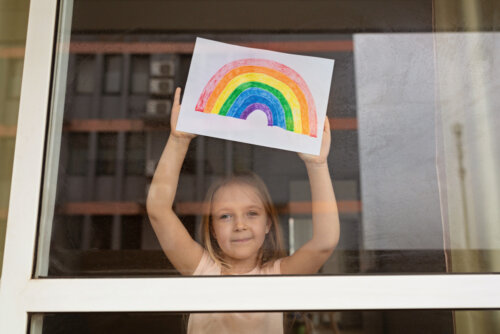 Niña con un dibujo de un arcoíris en la ventana de casa como muestra de que los niños son un ejemplo de adaptación.