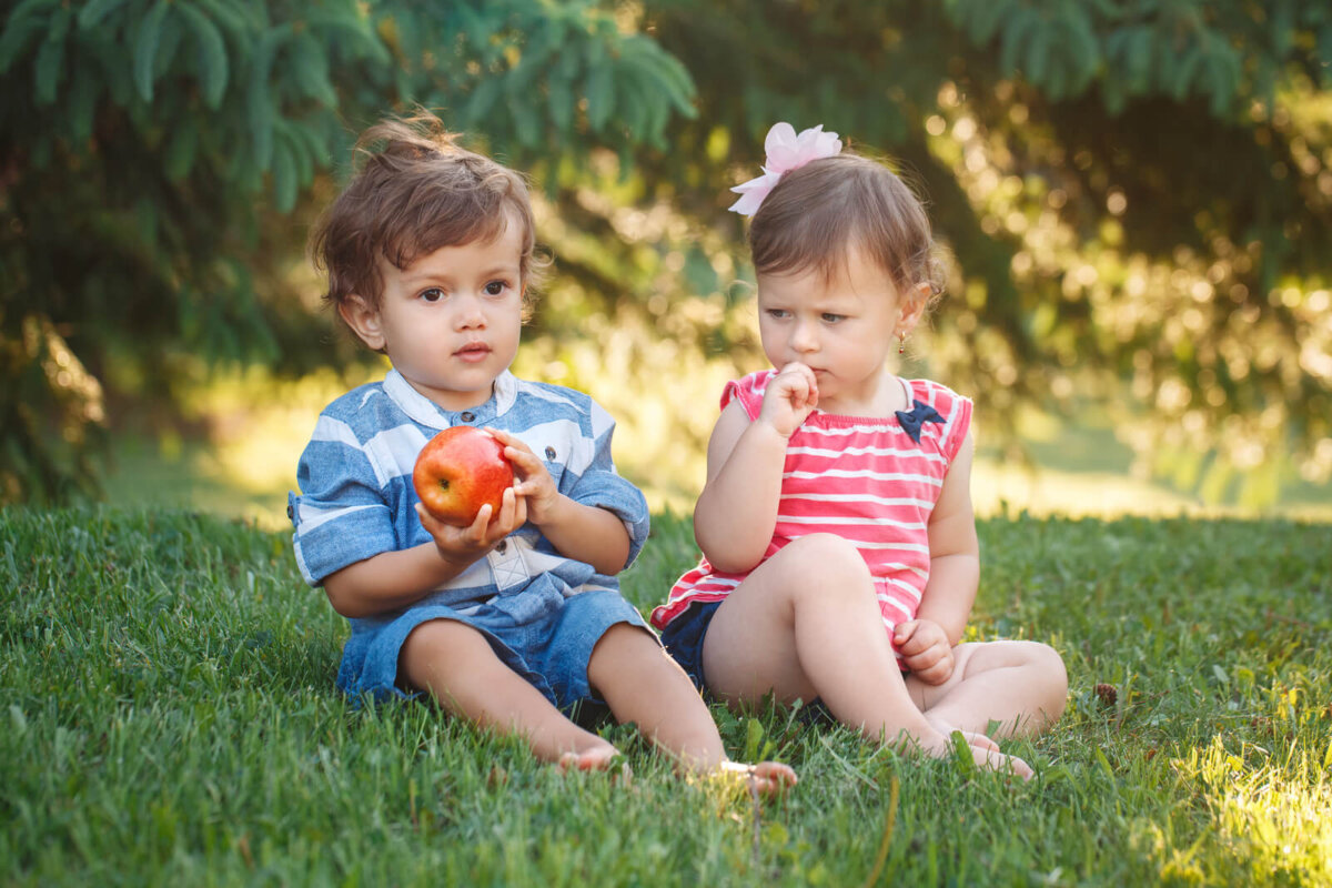 Niña teniendo envidia de su amigo porque tiene una manzana y ella no.