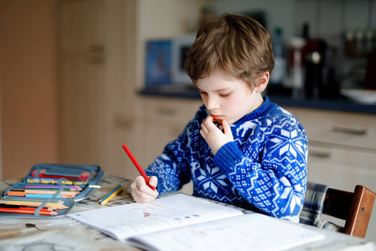 Niño haciendo deberes en casa sin tiempo libre, uno de los peligros de querer hijos perfectos.