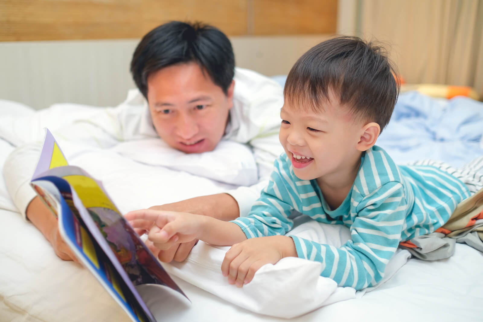 En far og hans småbarnssønn leser i sengen.