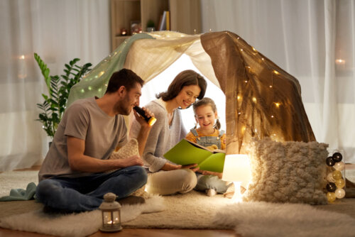 Padres leyendo con su hija en una cabaña construida en el salón de casa.