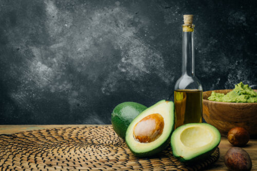 Botella de aceite de oliva y un aguacate, fuentes de grasas saludables.