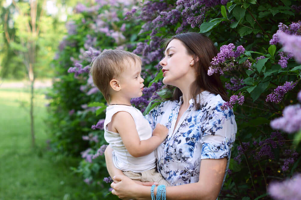 A mother standing near a lilac bush and talking to her toddler.
