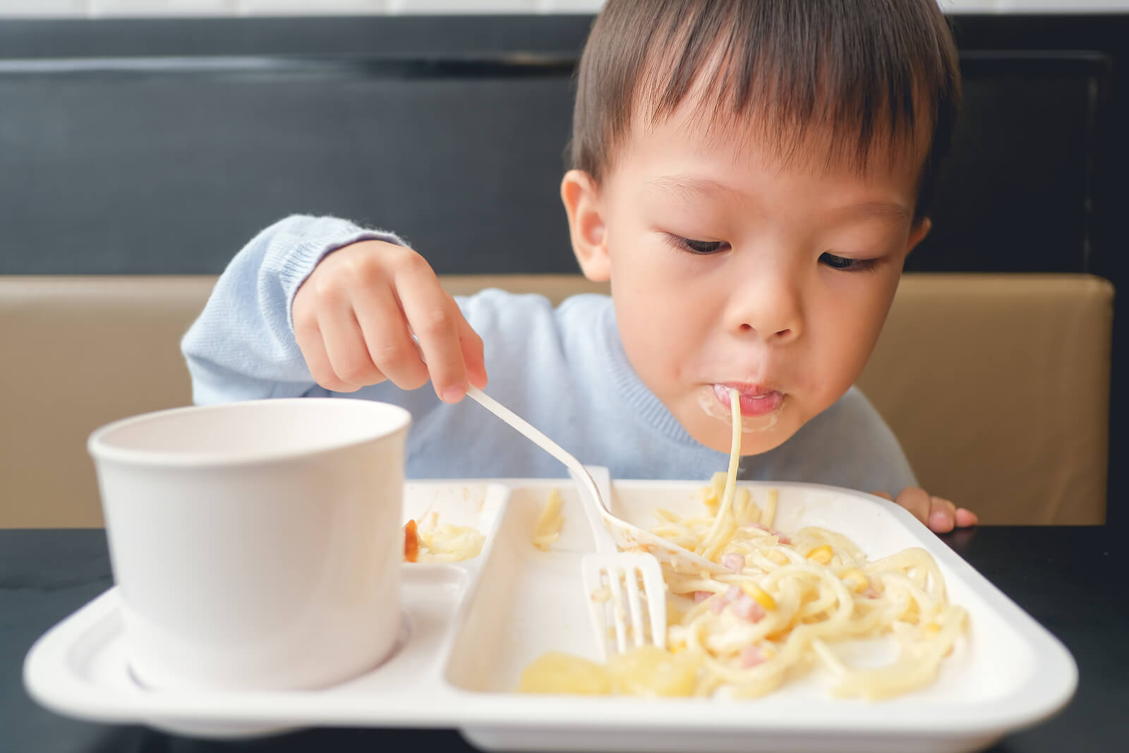Niño comiendo pasta carbonara incluida en su menú infantil.