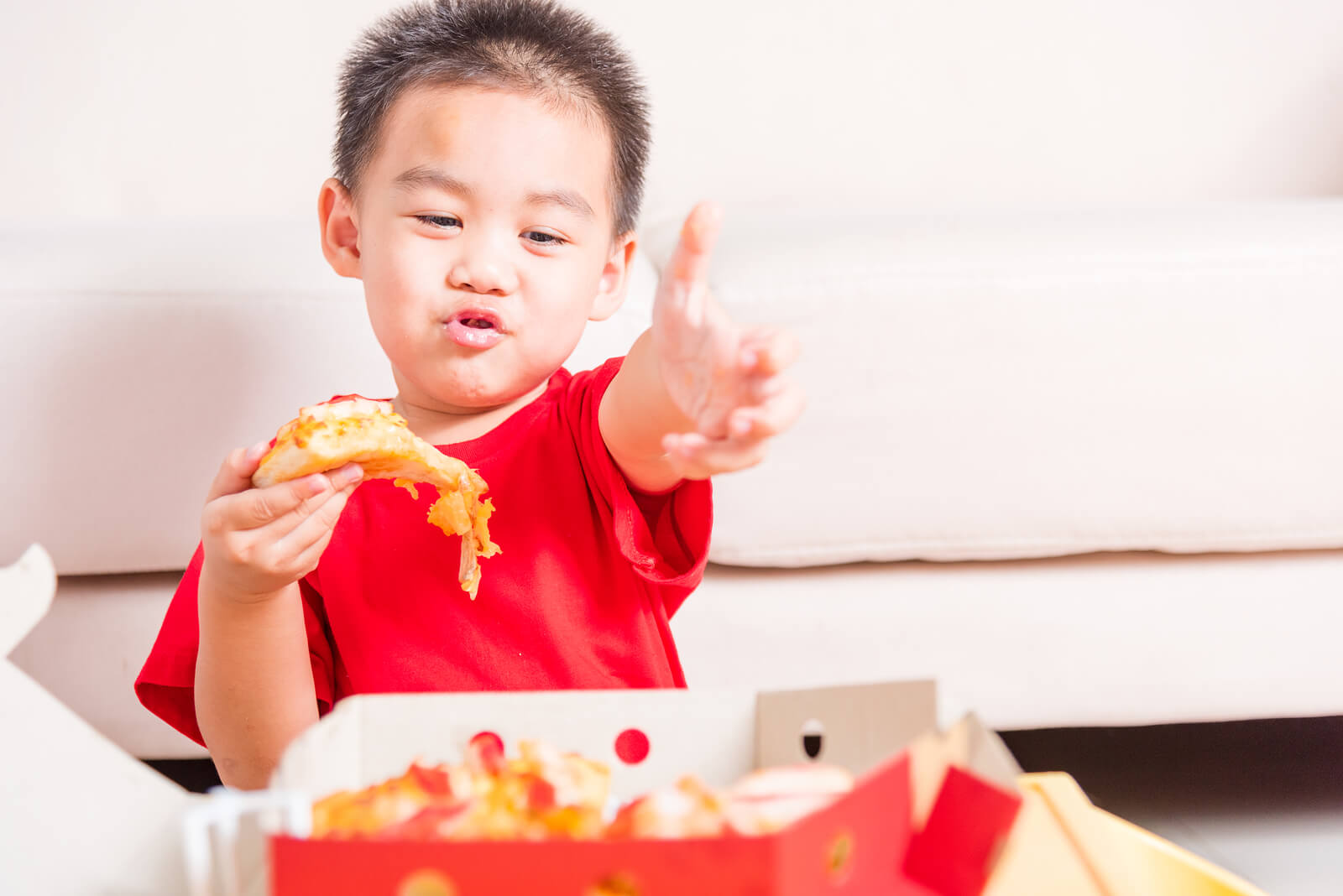 Niño comiendo pizza de un menú infantil, uno de los factores implicados en la regulación del apetito en niños.