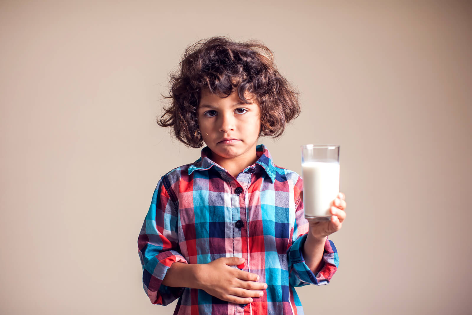 A child holding a glass of milk and rubbing his belly with an uncomfortable look on his face.
