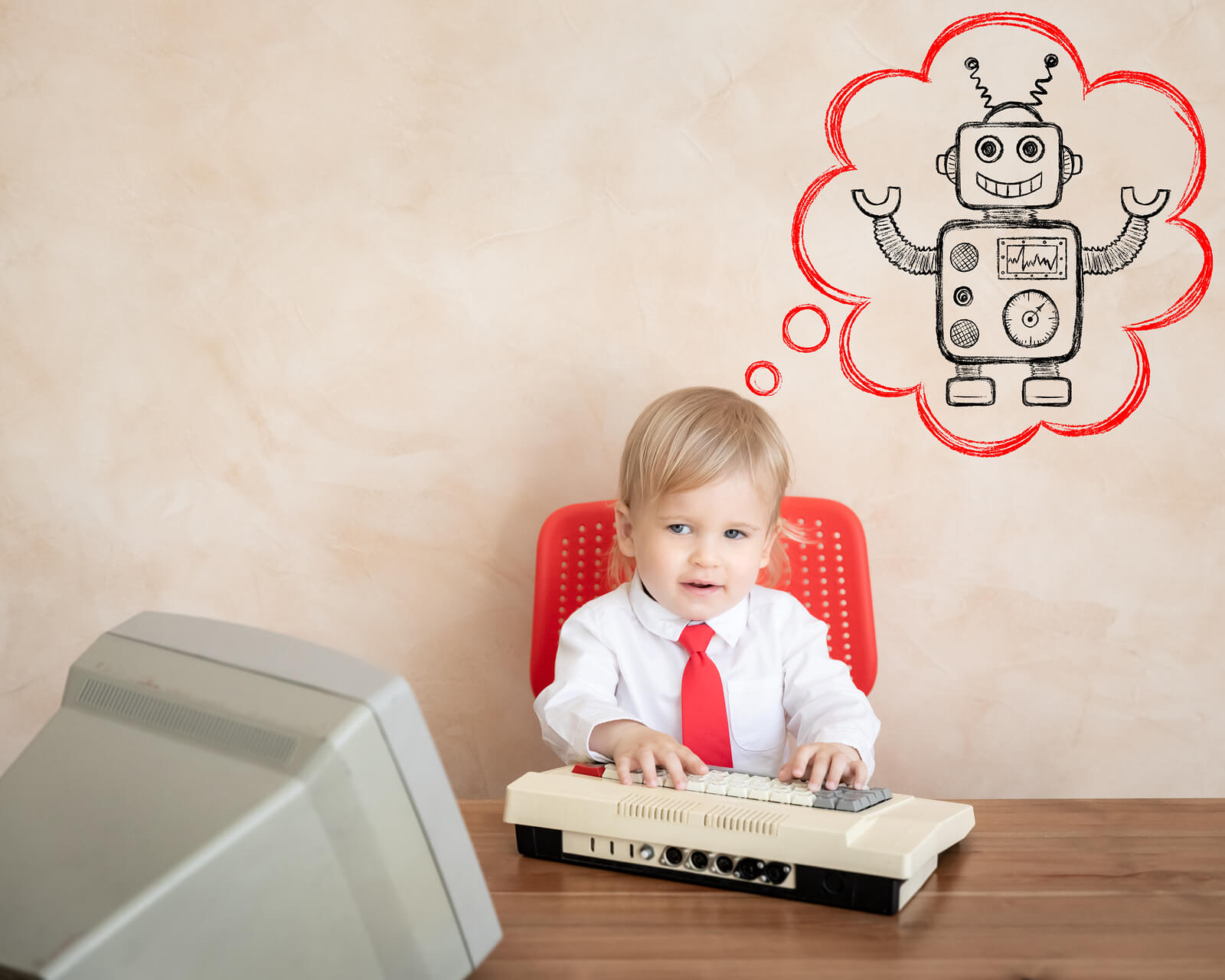 A toddler sitting on an old computer with a thought bubble over his head with a robot in it.
