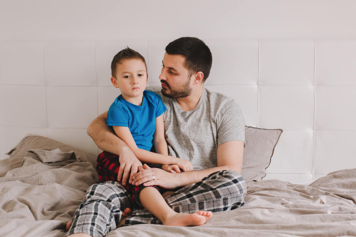 Padre hablando con su hijo sentados en la cama.