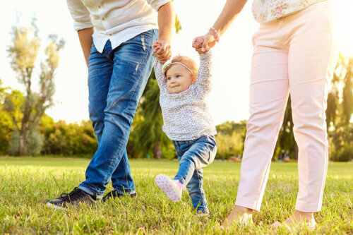 Bebé aprendiendo a caminar y dando sus primeros pasos cogido de las manos de sus padres.