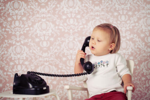 Niña pequeña hablando por un teléfono fijo.