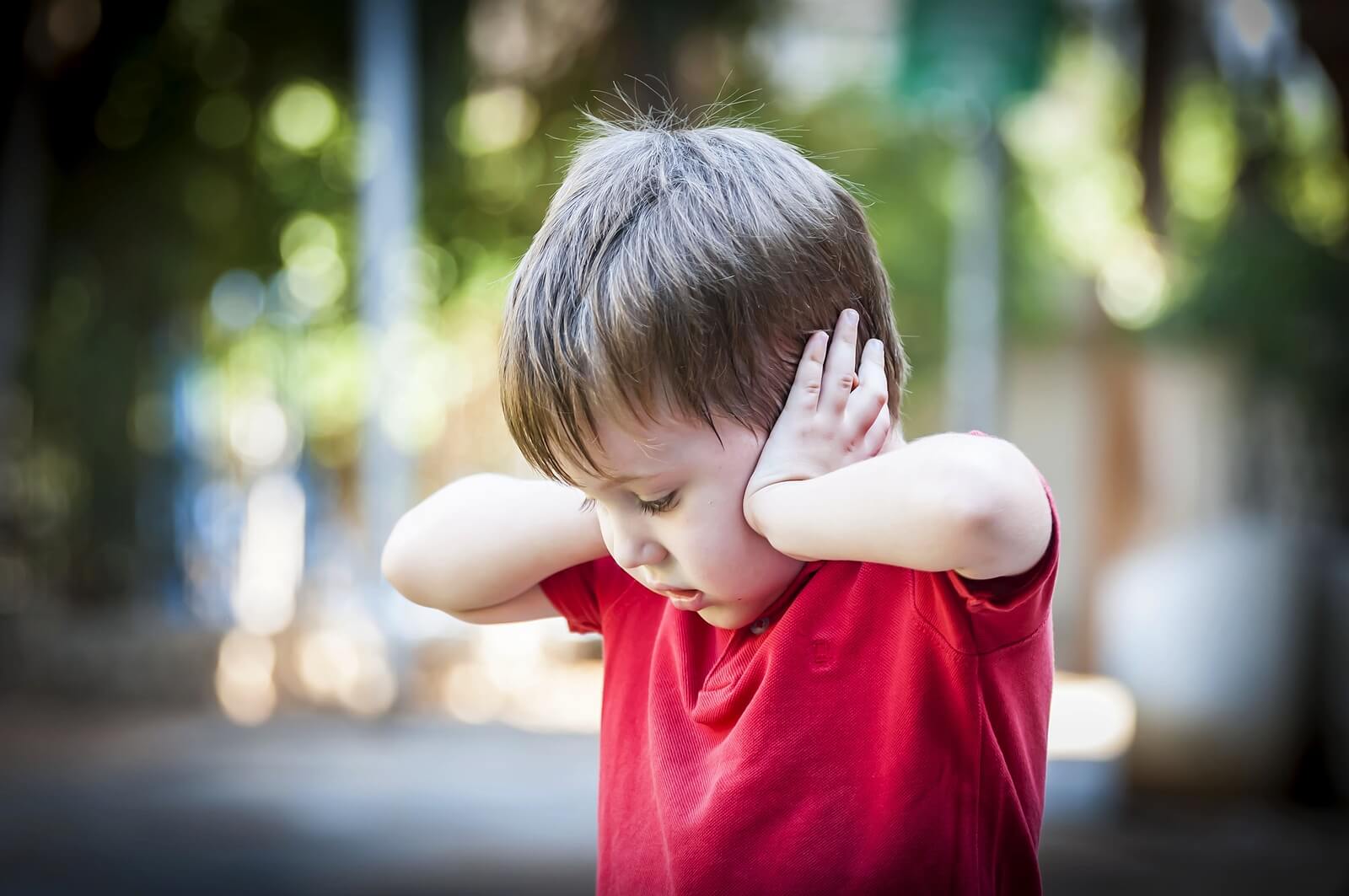 Niño asustado tapándose las orejas.