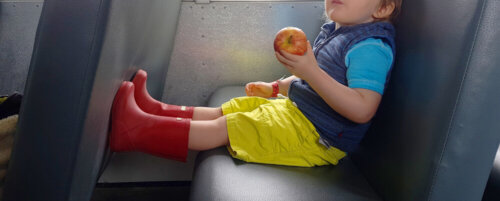 Niño comiéndose una manzana en el autobús con unas botas de agua.