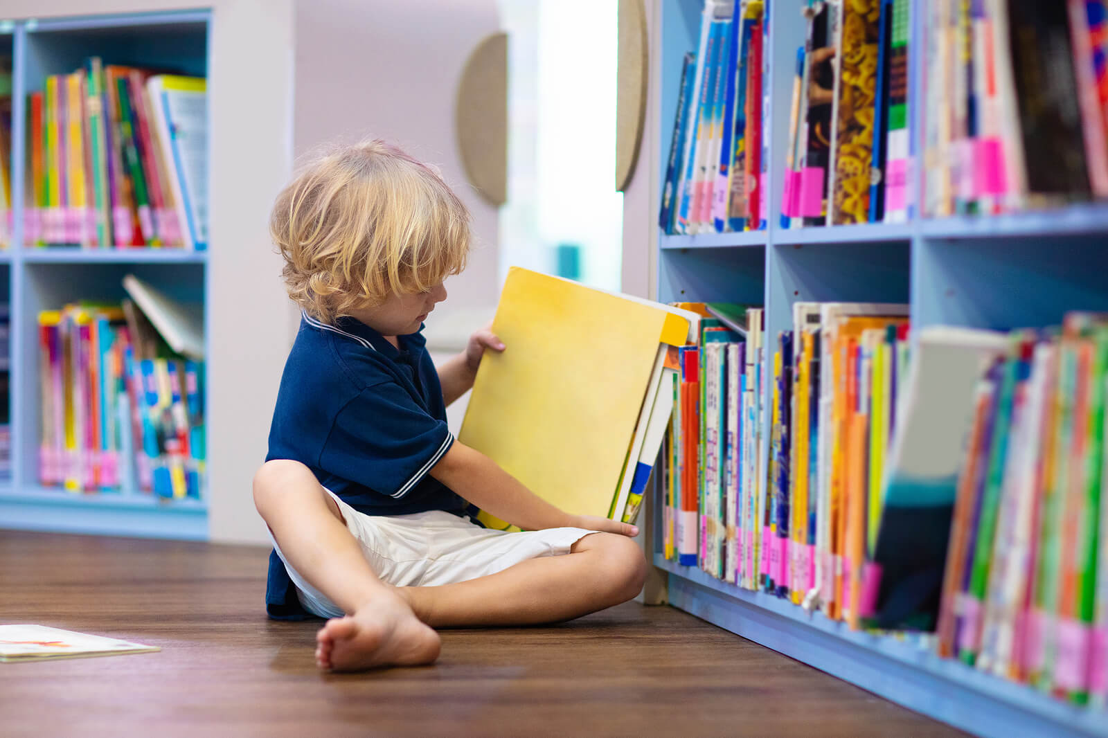 Niño cogiendo un libro y leyendo en la biblioteca de aula.