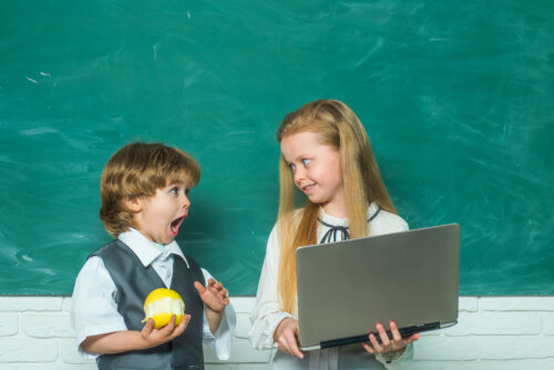 Niño con una manzana junto a su compañera de clase, que tiene un ordenador en las manos.