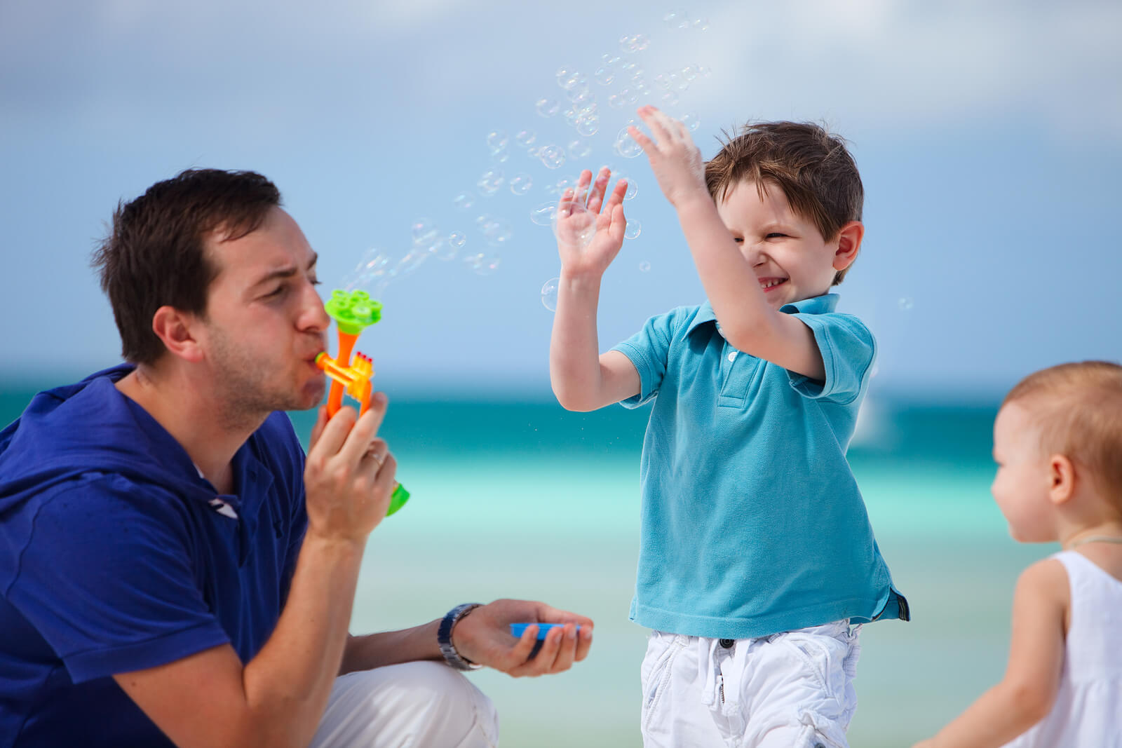 Padre jugando con sus hijos en la playa haciendo pompas de jabón.